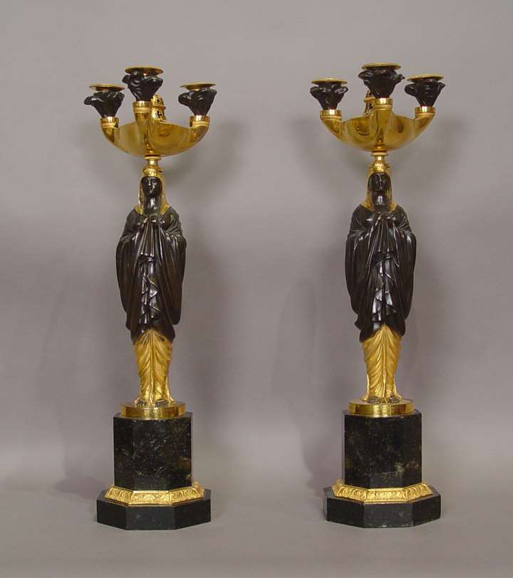 A Pair of Empire patinated and gilt-bronze candelabra, with “à l’antique” vestals supporting an oil lamp, on ormolu mounted pietra dura pedestals